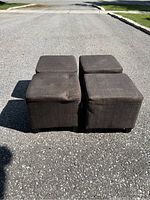Four brown fabric upholstered block stools arranged in pairs outside on pavement, showing top and side views.