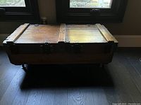 Closed view of wooden trunk coffee table showing top surface, metal hardware and legs