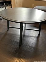 Photo showing side view of round dark green wooden coffee table with sturdy legs and horizontal braces underneath.