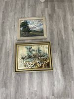 Two framed oil paintings laid on floor, one landscape, one abstract