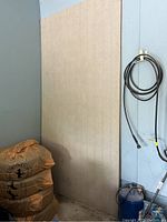 Two beige siding panels leaning against wall near equipment and bags. Panels measure approximately 8'x4'.