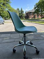 Full view of teal swivel desk chair showing seat, backrest, and base with wheels against outdoor background.