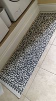 Photo of rectangular area scatter rug on tiled floor showing scroll and floral pattern in grey and white, positioned in front of laundry machines.