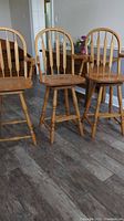 Three oak swivel bar stools positioned on a wood floor, showing front and side views with arrow style backs and hoop footrests.