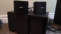 Large black Bose subwoofer with fabric front grille and two small cube Bose satellite speakers on top.