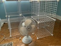 Set of white wire mesh storage cubes formed into approximately 9 units with connecting plastic clips, shown assembled on wooden floor alongside a white oscillating fan.