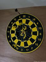Front view of the black and yellow dartboard with multiple darts stuck in it, some with yellow flights showing the wear and use.