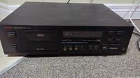 Front view of black Luxman stereo cassette deck with cassette slot, power and eject buttons visible.