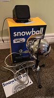 Blue Snowball microphone mounted on tripod stand with USB cable and external speaker, original blue and yellow Snowball box behind them