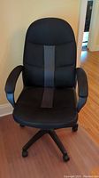 Front view of black adjustable office chair with padded armrests and caster wheels