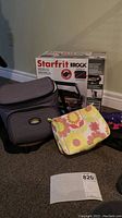 Photo showing Starfrit The Rock panini grill box, California Innovations lunch bag, floral cosmetic bag, and umbrellas placed on floor.