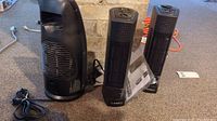 Photo of two Lasko ceramic tower heaters and one Sunbeam portable heater placed on carpeted floor near wall.