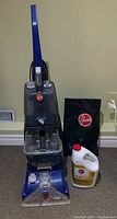 Full view of Hoover upright carpet cleaner, accessory bag, and cleaning solution jug on carpeted floor.