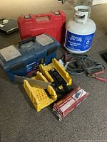 Overview of all items including red tool case, propane tank, jumper cables, mitre boxes with saw and foot pump.