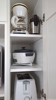 Photo of small appliances inside cabinet shelves including 5-cup coffee maker, coffee grinder, rice cooker, and toaster.