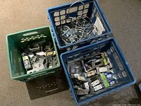 Three plastic crates containing assorted electrical hardware, switches, plugs, metal boxes, and hangers.