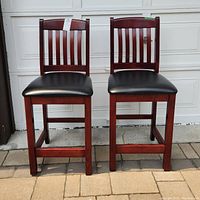 Front view of two wooden bistro chairs with black leather seats and slatted backs on outdoor patio.