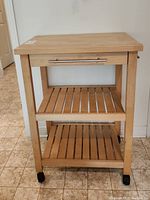 Front view showing butcher block top, drawer, and two slatted shelves with four black wheels