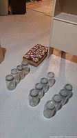 Mason jars and jam jars arranged on floor, 12 tall mason jars grouped in threes, 14 smaller jam jars in a cardboard box behind them.
