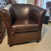 Front view of dark brown leather armchair showing curved backrest and seat cushion.