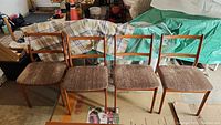 Four teak dining chairs in a row showing overall appearance and matching upholstery.