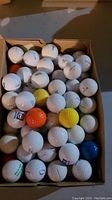 Photo of golf balls in a cardboard box showing various colors and some printed markings on balls