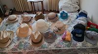 Top-down photo showing all hats and mitts laid out on a floral bedspread, featuring various summer hats, ball caps, and mitts