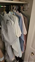 Photo of several men's large dress shirts hanging in a closet. Colors include blue, white, light pink, and striped patterns.