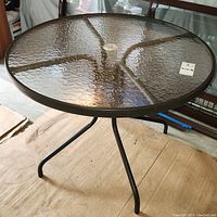 Front view of round outdoor table showing textured glass top and umbrella hole in center.