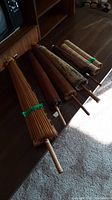 Photo showing five closed parasols laid side by side on a wooden surface, displaying their bamboo or wooden handles and ribs.