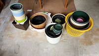 Group of assorted pots and containers arranged in multiple stacks and containers on a concrete floor.