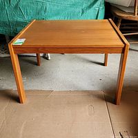 Front view of rectangular teak table showing its legs and tabletop with minor damage.