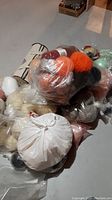 Photo showing multiple plastic bags containing balls of yarn in orange, black, white, and cream colors.