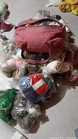Photo showing a collection of yarn balls and a pink fabric handbag on top, with yarn in plastic bags beneath.