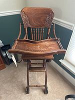 Front view of the antique high chair showing carved wooden backrest, tray, armrests, and front spindled supports.