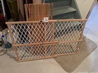 Photo of adjustable baby gate with wooden frame and white mesh on floor near stairs.