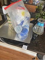 Photo showing a plastic bag containing blue and clear disposable plastic cups, a silver baking sheet underneath, and a flashlight with a blue handle.