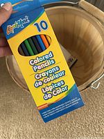 Box of Liquid Mark 10 colored pencils held over wooden barrel-style basket