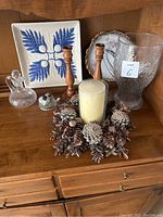 Overview of assorted decorative items on wooden surface including pinecone candleholder, candlesticks, plates, and glass pitchers.