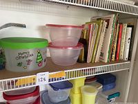 Shelf with various sizes and colors of plastic food storage containers with lids, including one with Christmas decorations.