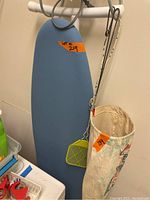 Ironing board, cloth bag with clothespins, and fly swatter hanging on board