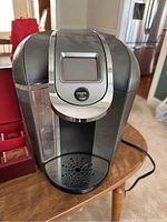 Front view of Keurig 2.0 coffee maker on table, showing touchscreen and water reservoir.