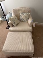 Beige lounge chair with vertical stripes and floral throw pillows from a front angle with matching ottoman visible.