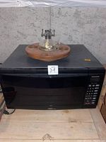 Photo showing a black Panasonic microwave with a wooden round base and glass kerosene lamp bottom on top.