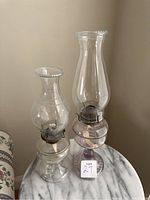 Both oil lamps on round marble-like table showing overall condition and size comparison.