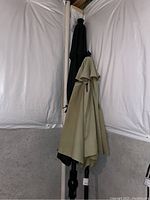Two outdoor patio umbrellas leaning against a white tent-like wall, one beige and one black, folded and closed.
