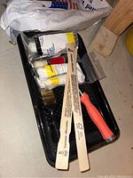 All painting supplies organized inside a black paint tray showing paints, brushes, mixing sticks, and roller handle.
