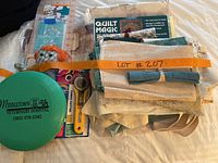 Top view of quilting fabrics folded and bundled with rotary cutter, scissors, measurement ruler, thread spools, and plastic organizer visible underneath.