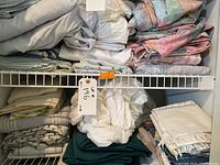 Multiple folded various sheets and linens in white, beige and pastel colors on two white wire shelves.