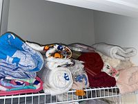 Folded and rolled assorted towels on a wire shelf, showing various colors and prints.